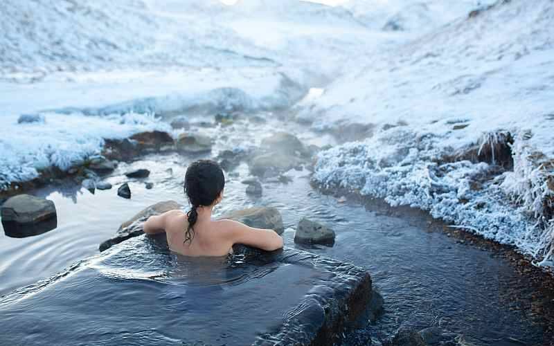 The girl bathes in a hot spring in the open air with a gorgeous view of the snowy mountains. Incredible iceland in winter.